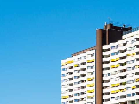 Torres do Wohnpark Alt-Erlaa, em Viena, com varandas brancas em curva e toldos amarelos sob céu azul limpo.
