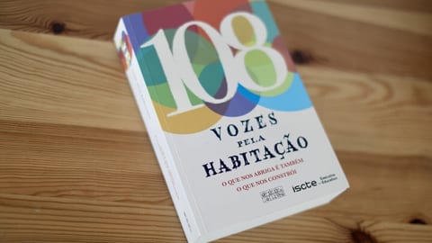 O livro 108 Vozes pela Habitação (Oficina do Livro), com o número 108 sobre círculos coloridos na capa, sobre uma mesa de madeira.