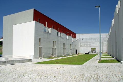 Bairro da Bouça, Porto, de Álvaro Siza (operação SAAL): bandas de habitação brancas com o piso superior vermelho-escuro e empenas de betão, alinhadas sobre um relvado comum com pavimento de cubos de granito.